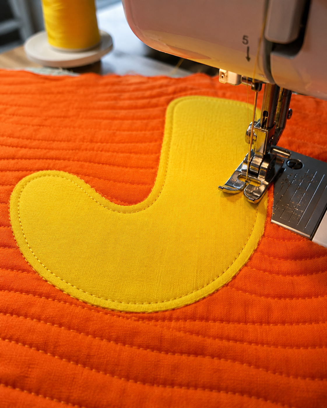 Sewing the JOY quilt letter J — machine stitching yellow appliqué onto orange background fabric